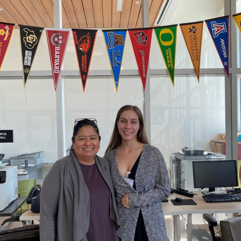SCDC Director Emma Hernandez poses for a photo with a intern below a colorful college banners.