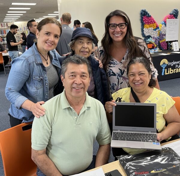 a family of five adults who have just been the recipients of new laptop smiling for a photograph with their new computer.